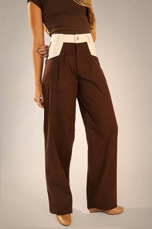 Modelo usando calça alfaiataria marrom com recorte no bolso diagonal, tecido 100% algodão e estilo atemporal.