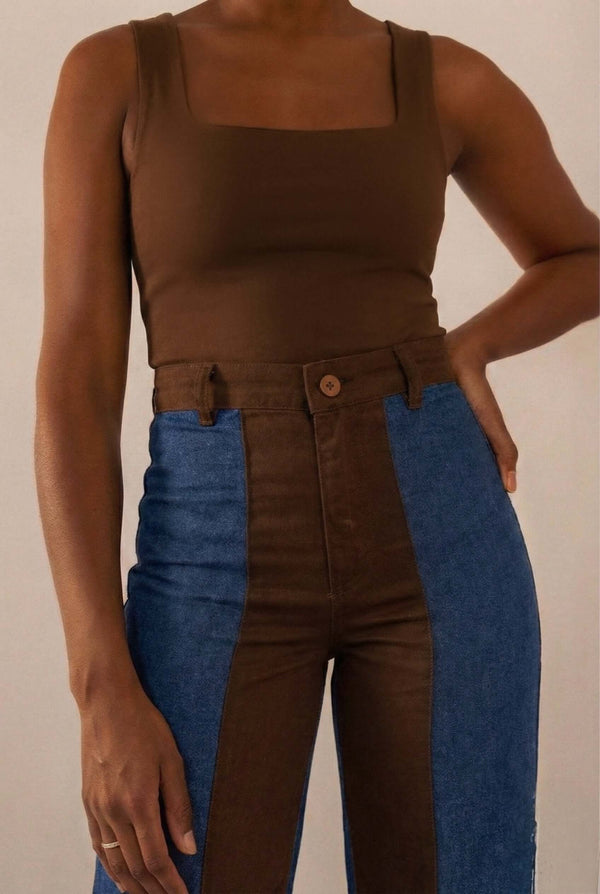 Calça Bicolor Jeans com Marrom, apresentando recorte vertical entre denim azul e marrom, combinada com top marrom.